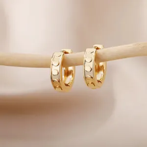 Close-up of golden hoop earrings with embossed dot patterns on a wooden branch