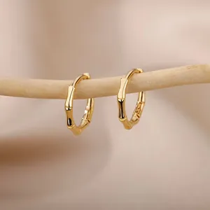 Macro view of gold-plated bamboo-shaped hoop earrings hanging on a natural wooden branch