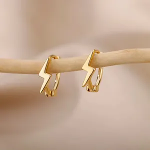 Close-up of golden lightning bolt charm hoop earrings hanging on a decorative branch