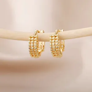 Macro detail of gold hoop earrings with mesh texture hanging on a wooden branch