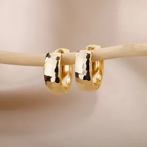 Macro detail of gold hammered texture thick hoop earrings hanging on a branch