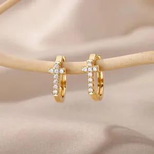 Golden hoop earrings with sparkling zircon cross pendants on a silk background