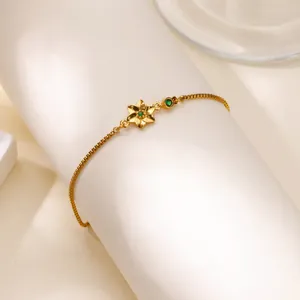 Détail d'un bracelet à pendentif fleur dorée avec pierres précieuses vertes sur support blanc