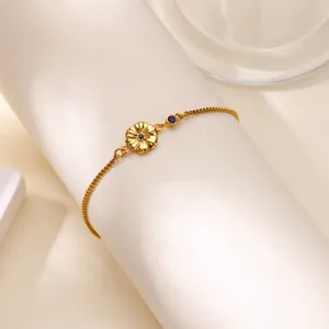 Gros plan du bracelet doré avec pendentif fleur et cristaux bleus sur support blanc