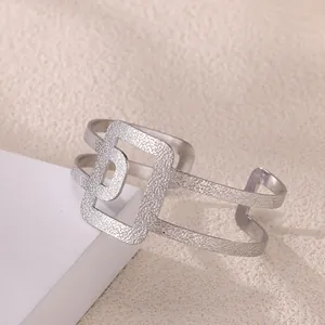 Detalle de brazalete plateado con diseño geométrico calado en soporte blanco