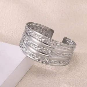 Detalle del brazalete abierto de acero inoxidable plateado con texturas trenzadas y pulidas