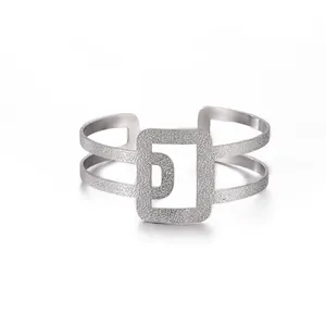 Detalle de brazalete abierto de acero inoxidable plateado con textura martillada y forma de D