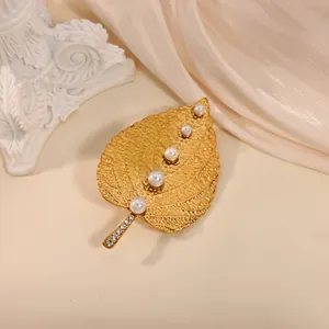 Elegant gold leaf brooch with pearls and rhinestones on soft silk background