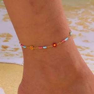 Colorful summer anklet with gold chain and zircon floral charms on a beach setting