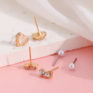 Detalle de pendientes dorados con opalo de corazón, lazo de cristal y perlas sobre seda