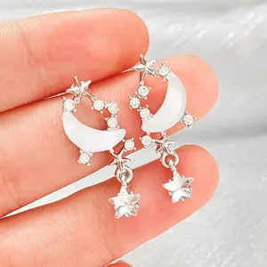 Macro view of silver moon and star earrings with sparkling stones held by hand