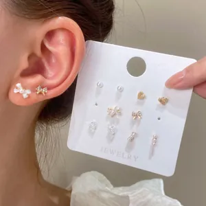 Primer plano de un set de pendientes de plata con motivos de mariposa y corazón en modelo