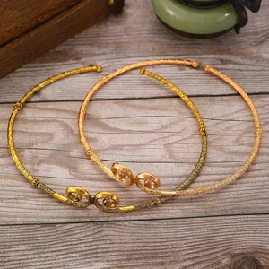 Detail of golden brass open bangles with intricate lucky cloud carvings on wood base