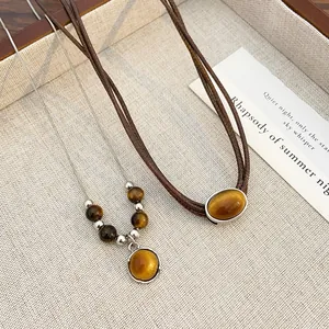 Detail of tiger eye stone necklaces with silver chain and brown braided cord on a tray