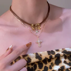Close-up of double-layered star and cross necklaces on neck with brown leather choker