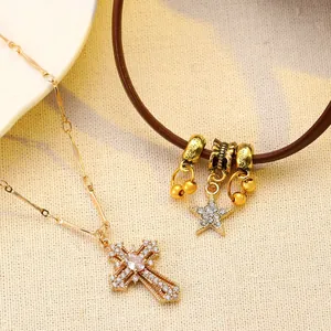 Detail of layered gold cross pendant and star charm on dark brown leather cord necklace