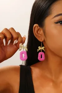 Close-up of golden bow earrings with pink floral heart pendants shown on a model