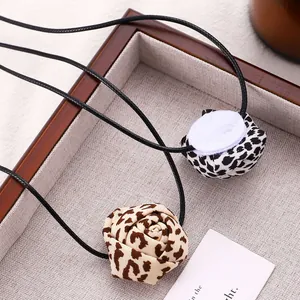 Macro shot of leopard print fabric rose and button pendant on a black cord necklace
