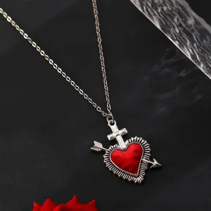 Macro shot of red heart pendant with silver cross and cupid arrow on a snake chain