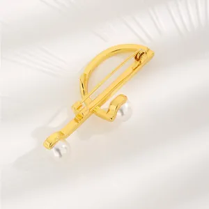 Elegant geometric gold brooch with white pearls displayed on textured white background