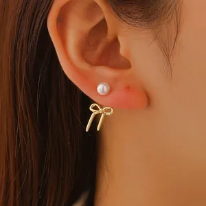 Close-up of elegant bow earrings with round white pearls and gold-tone finish on model