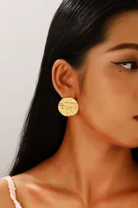 Close-up of golden stainless steel earrings featuring irregular textured melted lava surface