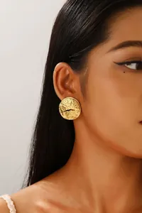 Detail of gold round earring with irregular lava texture worn by a model