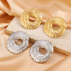 Detail of irregular textured hoop earrings in gold and silver finish on silk fabric