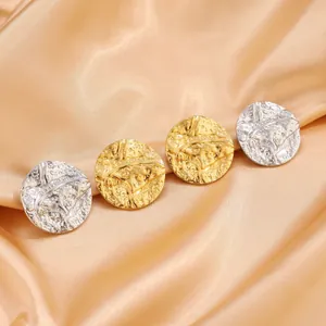 Detailed close-up of gold and silver hammered stainless steel earrings on satin fabric