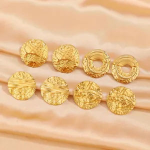 Detailed macro view of gold stainless steel earrings with textured hammered finish on satin silk