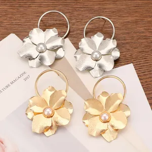 Detalle de pendientes de flores de metal cepillado con adorno de perla central