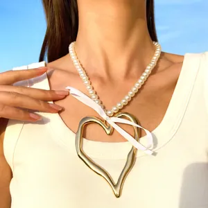 Détail d'un grand pendentif cœur doré sur un collier de perles blanches avec ruban
