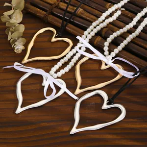 Détail de grands pendentifs en forme de cœur creux doré et argenté avec chaîne de perles