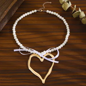 Detail of pearl necklace featuring a large golden heart pendant and elegant white ribbon bow