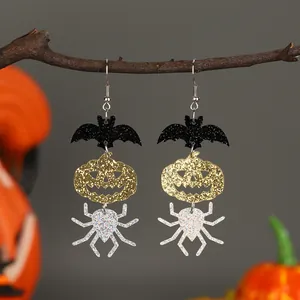 Detail showing glittery bat, pumpkin, and spider layered drop earrings on wood