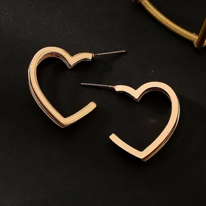 Detailed view of large gold-toned heart-shaped hoop earrings on a black background