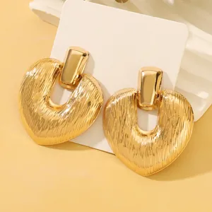Detailed view of large golden heart earrings with textured brushed metal finish on cards