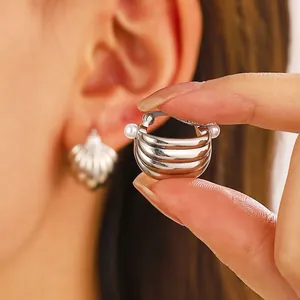 Pendientes de aro plateados con rayas y detalles de perlas sostenidos con la mano