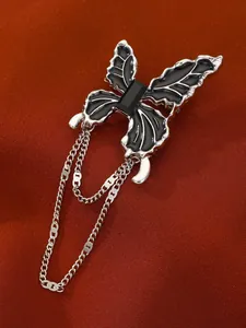 Close-up of a dark butterfly brooch with black enamel, crystal stone, and metal tassels