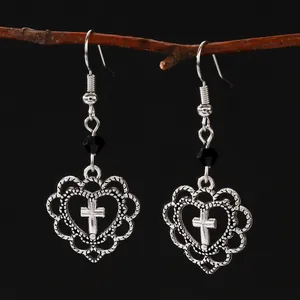 Macro detail of gothic silver heart earrings with cross hanging on a natural branch