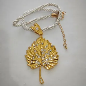 Detail of gold leaf pendant with crystal rhinestones on a white twisted rope necklace
