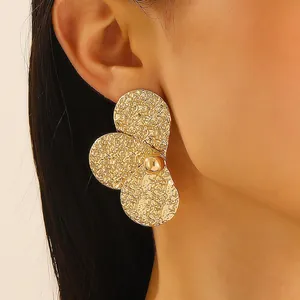 Close-up of oversized gold flower earrings with hammered texture and center bead on model