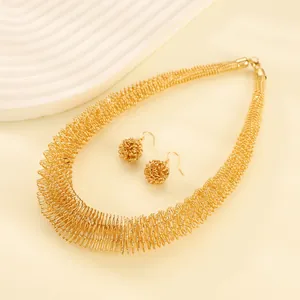 Detailansicht der goldenen Spiral-Halskette und Kugel-Ohrringe auf strukturiertem Grund