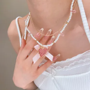 Detailed view of double-layer pearl necklace with pink enamel heart and bow on collarbone
