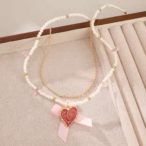 Detail of double-layer necklace with pearls, pink heart pendant and satin bow charm