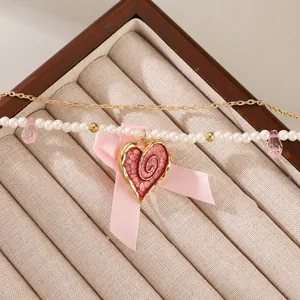 Detail of pearl necklace featuring red enamel heart pendant and pink silk bow tie