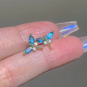 Makroaufnahme von Gold-Libellen-Ohrringen mit blauen Zirkonia-Steinen auf dem Finger