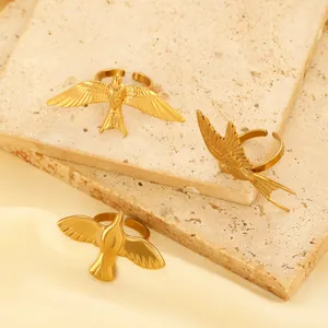 Detailed close-up of golden swallow bird open rings on warm toned stone and fabric