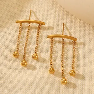 Detail of gold fringe earrings featuring hanging chains and spherical polished pendants