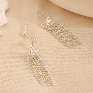 Detail of silver stainless steel bow tassel earrings on a textured fabric background